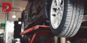 ماشین مشکی برروی جک بالابر تعمیرگاه با نمای نزدیک از لاستیک جلو و لوگوی داداشی تایر در گوشه تصویر