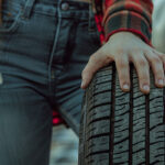 خانمی کنار ماشین درحال نگه داشتن یک لاستیک