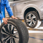 مرد درحال هل دادن لاستیک ماشین با رینگ نقره ای رنگ