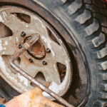 مکانیک در حال محکم کردن مهره های چرخ ماشین با آچار