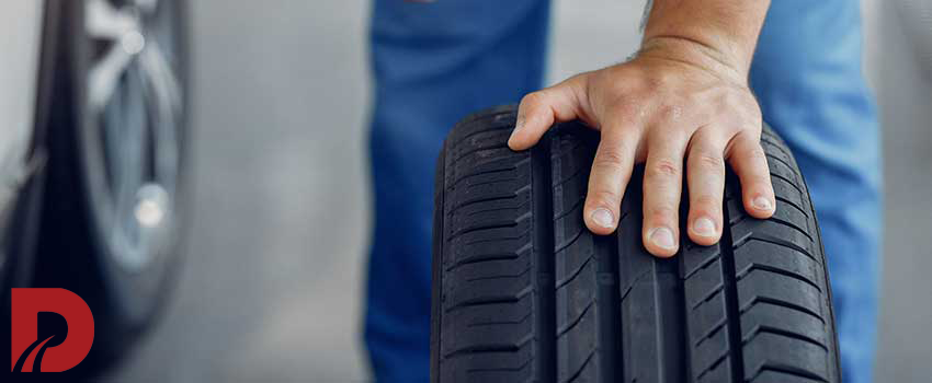 نکانیک با لباس کار آبی یک لاستیک را نگه داشته است