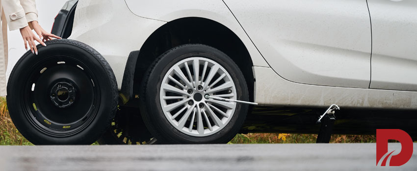 خانم درحال هل دادن لاستیک ژاپاس کنار ماشین پارک شده کنار جاده